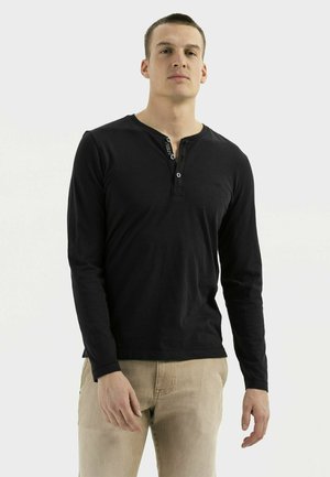 Zwarte long-sleeve shirt met een knoopsluiting bij de hals en textuur details, gecombineerd met lichtbeige broeken.