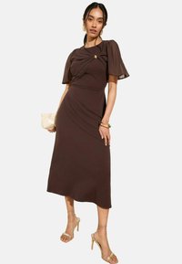 Abito midi marrone con maniche a sbuffo corte e dettaglio sul corpetto arricciato. Presenta una silhouette fluida e una texture liscia.