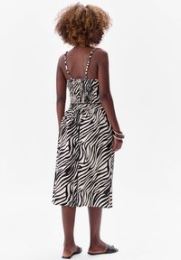 Czarna i kremowa w paski midi sukienka z marszczonym gorsetem i cienkimi ramiączkami, z luźną spódnicą i detalem na plecach. Noszona z czarnymi sandałami.