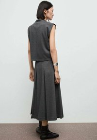 Ensemble gris en deux pièces composé d'un haut court sans manches et d'une jupe midi plissée, fabriqué dans un tissu doux. Des bottines noires à la cheville sont portées.