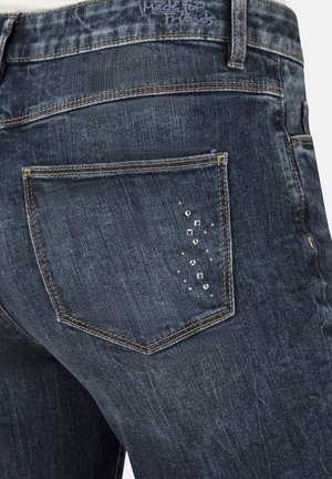 Dark blue denim jeans featuring a back pocket with silver embellishments, distressed texture, and contrast stitching along the edges.