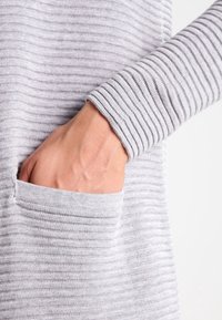 Hand geplaatst binnenzak van een lichtgrijze ribgebreide trui-sleeve.