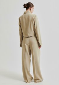 Beige rutig kostym med en skräddarsydd kavaj och vida byxor. Slätt tyg, minimal hårdvara och en figurnära midja med detalj av bälte på ryggen.