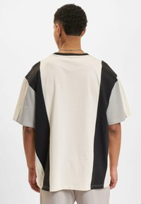 Oversized T-shirt in cream, black, and gray colors. Features color-block design with contrasting panels and a soft cotton texture.