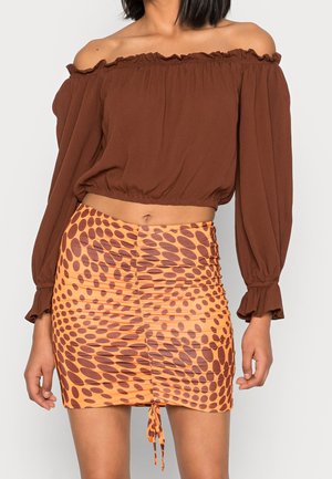 Woman wearing a brown off-shoulder long-sleeve top and a ruched orange mini skirt with brown oval patterns.
