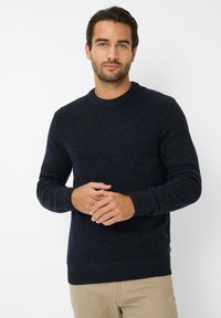 Granatowy sweter z prążkowanej dzianiny z okrągłym dekoltem, z fakturowaną górną częścią i jednolitą dolną sekcją, w komplecie z jasnobeżowymi spodniami.