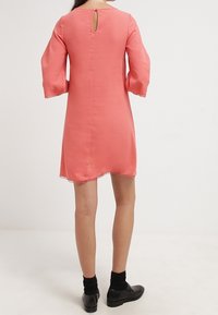 Korálové šaty s rukávy po lokty, detailem klíčové dírky na zádech, vlnkovaným lemem a hladkým materiálem. Nosené s černými punčochami a botami.