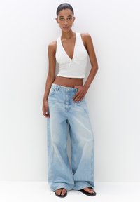 Biely rebrovaný crop top s nastaviteľným viazaním vpredu, kombinovaný s oversized svetlomodrými džínsami s širokými nohavicami a jemnými detailmi šitia.