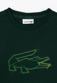 T-shirt in cotone verde scuro con logo Lacoste ricamato geometrico in giallo e verde brillante, con un classico design a girocollo.