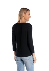 Czarny top z długim rękawem i zaokrąglonym dekoltem, wykonany z miękkiego materiału. Posiada luźny krój, pokazany w połączeniu z jasnoniebieskimi dżinsami.