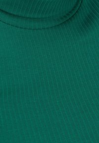 Vihreä ribbikangas, jossa on korkea kaulus, näyttää pystysuuntaisen neuleen rakenteen ja ryppyjä kaula-aukossa.