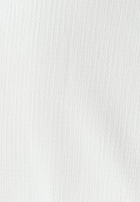 Bela teksturirana tkanina z nežnimi valovitimi vzorci, lahka, z rahlo dvignjeno površino, ki ustvarja mehki vizualni učinek.