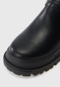 Čierna kožená členková obuv s hladkou textúrou, zaoblenou špičkou a hrubou, robustnou podrážkou s výrazným vzorom dezénu.