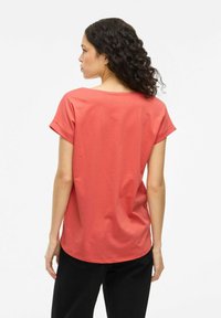 T-shirt corallo a maniche corte realizzato in morbido cotone. Vestibilità comoda con scollatura rotonda e maniche arrotolate, abbinato a pantaloni neri.