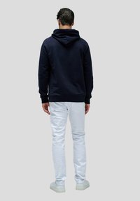 Felpa navy con finitura testurizzata, dotata di un grande cappucci, polsini e orlo a costine. Abbinata a jeans slim-fit bianchi e sneakers.