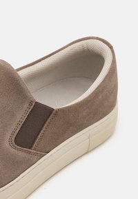 Zapato sin cordones en ante topo que presenta acentos elásticos laterales, un forro interior texturizado y una suela de goma de color claro. Diseño de punta redondeada.