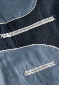 Een gestructureerde marineblauwe stof met lichtblauwe secties, gekenmerkt door krijtstrepen en stippen, accenten van witte piping en functionele lussen.