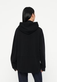 Sudadera negra de gran tamaño con capucha, mangas largas y textura suave. Presenta un corte recto y costuras mínimas. Adecuada para uso casual.