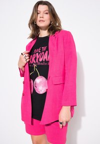 Rosa linneskjorta över en svart t-shirt med grafisk design som har rosa discokulor. Matchas med rosa skräddarsydda shorts. Silverringar accentuerar looken.