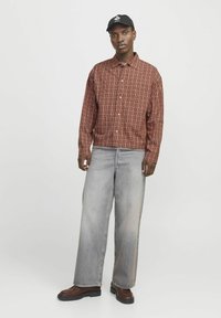 Bruin geruite knopshirt met een kraag, gedragen over lichtgrijze wijde jeans. Bruine schoenen met een gestructureerde zool. Zwarte pet.