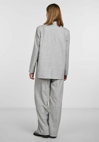 Szara marynarka o luźnym kroju oraz pasujące do niej spodnie z teksturowanej tkaniny. Marynarka ma prosty krój z centralnym szwem i bez widocznych zapięć.