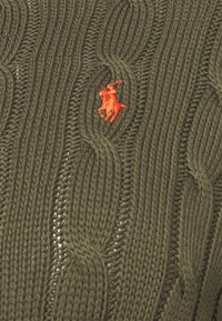 Tissu tricoté en câble de couleur vert olive avec une petite broderie orange détaillée d'un joueur de polo à cheval au centre.