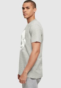Camiseta de algodón gris con un gran diseño gráfico blanco en la parte delantera. Manga corta, cuello redondo, corte relajado y textura suave.