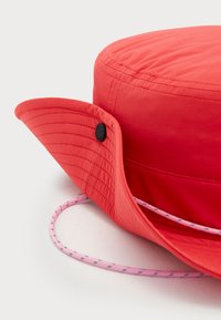Chapeau en seau rouge en tissu léger avec une couronne arrondie et un large bord flexible. Présente un cordon rose avec des coutures décoratives.