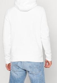 Sudadera blanca con capucha y bolsillo canguro, puños y dobladillo acanalados. Usada con shorts de mezclilla azul claros. Textura de tela suave.