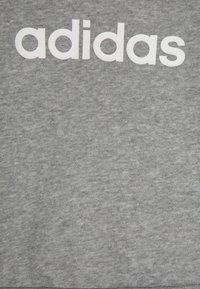 Pilkas medvilnės džemperis, ant krūtinės su dideliu baltu "adidas" logotipu. Audinys turi minkštą, tekstūruotą išvaizdą.