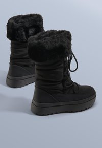 Czarne zimowe botki z grubym, teksturowanym futrzanym mankietem, wyściełanym korpusem oraz gumową podeszwą. Posiadają sznurowanie i lekko podwyższoną platformę.