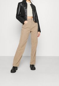 En svart läderjacka i kort modell över en ljus beige topp, tillsammans med högmidjade, texturerade beige kordbyxor och kraftiga svarta stövlar.