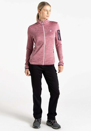 Pullover-Jacke aus leichtem rosa melierten Stoff, mit Reißverschluss vorne, Stehkragen, zwei seitlichen Taschen und schwarzen Akzenten an den Ärmeln sowie dunklen Hosen.