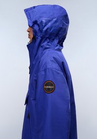 Blue waterproof jacket featuring a hood, sleek design, and a badge on the left sleeve. Smooth texture with visible seams and zippers.