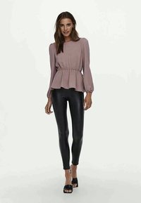 Ljust rosa peplumtopp med långa puffärmar och dragsko i midjan, kombinerad med svarta glansiga leggings och svarta slidesandaler.