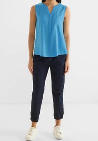 Blå ärmlös blus med V-ringning, två bröstfickor, matchad med marinblå tapered-byxor och vita sneakers. Slätt tyg med en avslappnad passform.