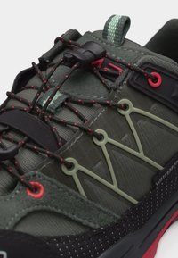 Gros plan sur une chaussure de randonnée imperméable verte et noire avec des lacets élastiques accentués de rouge et une languette de maintien sur la languette.