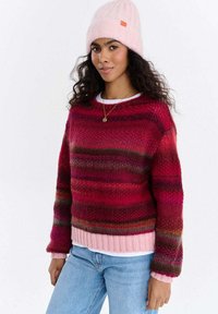 Sweter dziergany z poziomymi paskami w odcieniach czerwieni, różu i brązu. Posiada prążkowany dół, okrągły dekolt i luźny krój. W zestawie z różową czapką typu beanie.