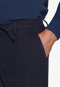 Marineblaues Hosen aus glattem, strapazierfähigem Stoff mit lockerer Passform. Verfügt über einen elastischen Taillenbund und Seitentaschen. Darüber ein strukturiertes blaues Sweatshirt.