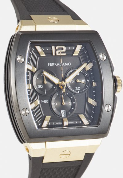 Hodinky Ferragamo F-80 s čiernym obdlžnikovým puzdrom, zlatými akcentmi, textúrovaným čiernym gumovým remienkom a tromi subčíslami na čiernom ciferníku.