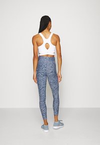 Vit sport-bh med en nyckelhålsöppning, i kombination med höga blå leggings med ett strukturerat bladmönster. Blå sportskor.