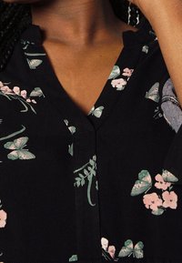 Tela negra con un diseño floral que presenta flores rosas y hojas verdes, destacando un escote en forma de V y acentos texturizados.