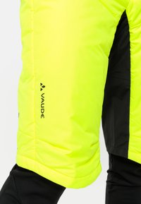 Geïsoleerde gele shorts met zwarte accenten, met een gestikte textuur en een zichtbaar logo. De stof lijkt duurzaam en weerbestendig.