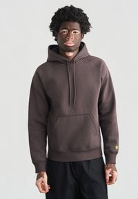 Καφέ φούτερ με κουκούλα, με μπροστινή τσέπη και μακριά μανίκια· διαθέτει λογότυπο στο μανίκι και μαλακό, υφή ύφασμα.