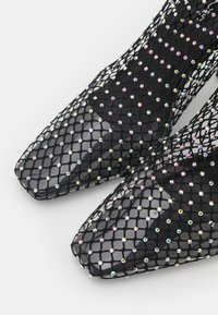 Stivaletti alla caviglia in rete nera con un motivo a diamante, caratterizzati da strass colorati e design con punta affusolata. Fodera interna liscia.