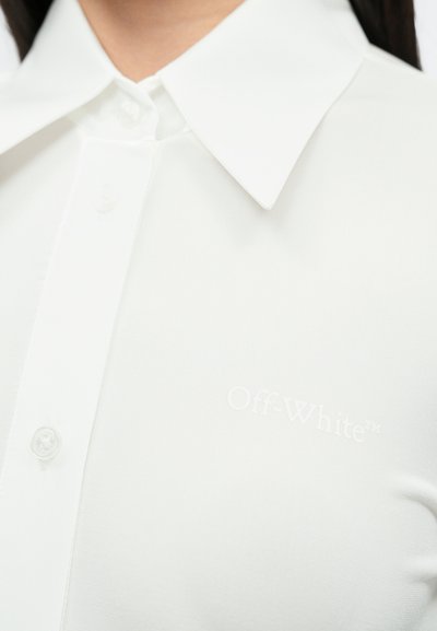 Balta marškiniai su klasikinio tipo apykakle, pagaminti iš lygaus audinio. Apatinėje dalyje yra subtilus Off-White logotipas, aiškūs mygtukai.