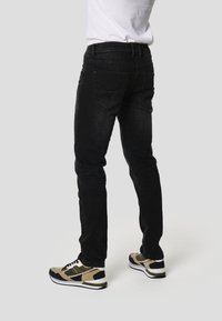 Mørkeblå denimjeans med smal pasform, der har baglommer, kombineret med brune og sorte sportsudstyrssko. Stoffet har en let struktur.