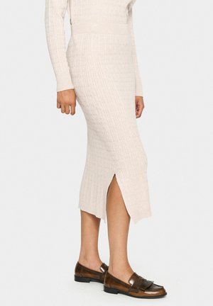 Gonna midi a costine beige chiaro con uno spacco laterale, abbinata a mocassini marrone scuro con dettaglio frangiato. Tessuto liscio e design aderente.