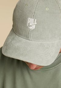 Couvre-chef en velours côtelé de couleur vert clair avec une surface texturée, un bord incurvé et un logo "PULL IN" brodé en blanc à l'avant.