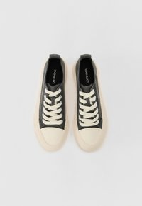 Graue Leinenschuhe mit weißer Gummi-Zehenschutzkappe und -sohle, ausgestattet mit weißen Schnürsenkeln und einer Schlaufe hinten für einfaches An- und Ausziehen. Flaches Design.